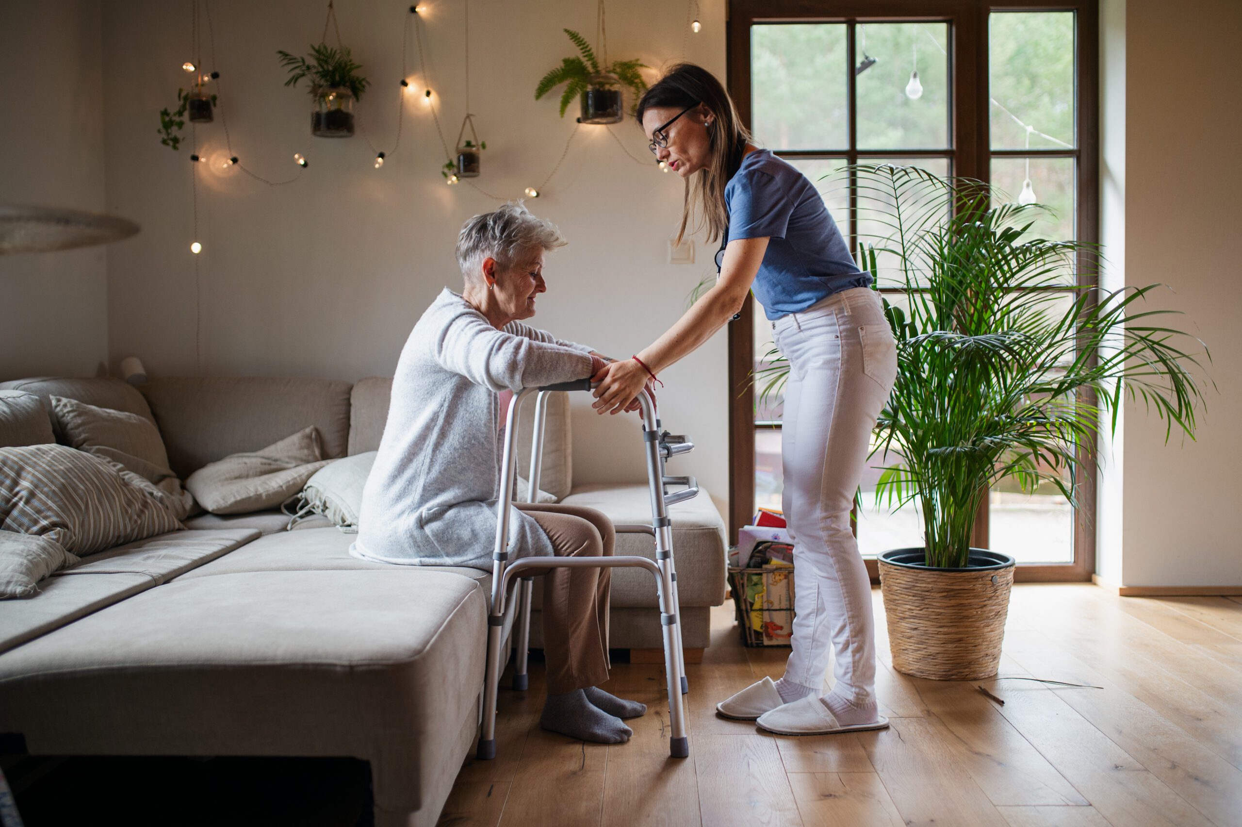 Woman assisting senior with a walker from bed