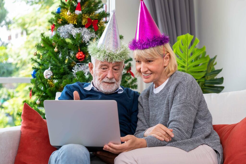 senior-couple-using-laptop-video-phone-call-greeting-their-family-christmas-festival-sitting-sofa-with-decoration-tree