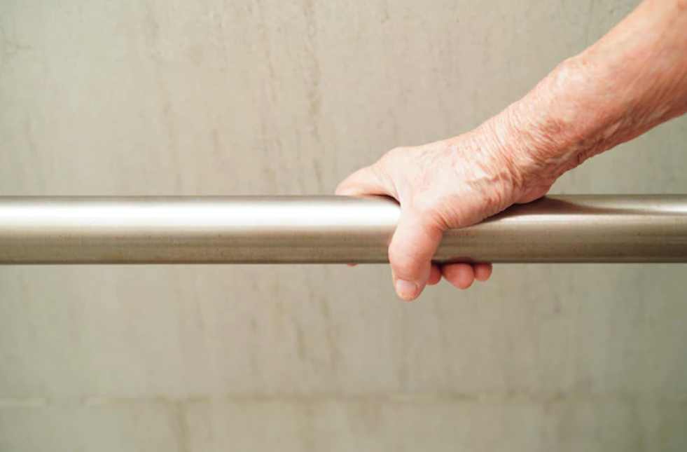 A senior citizen's hand holding a hand rail in a shower getting ready to bathe