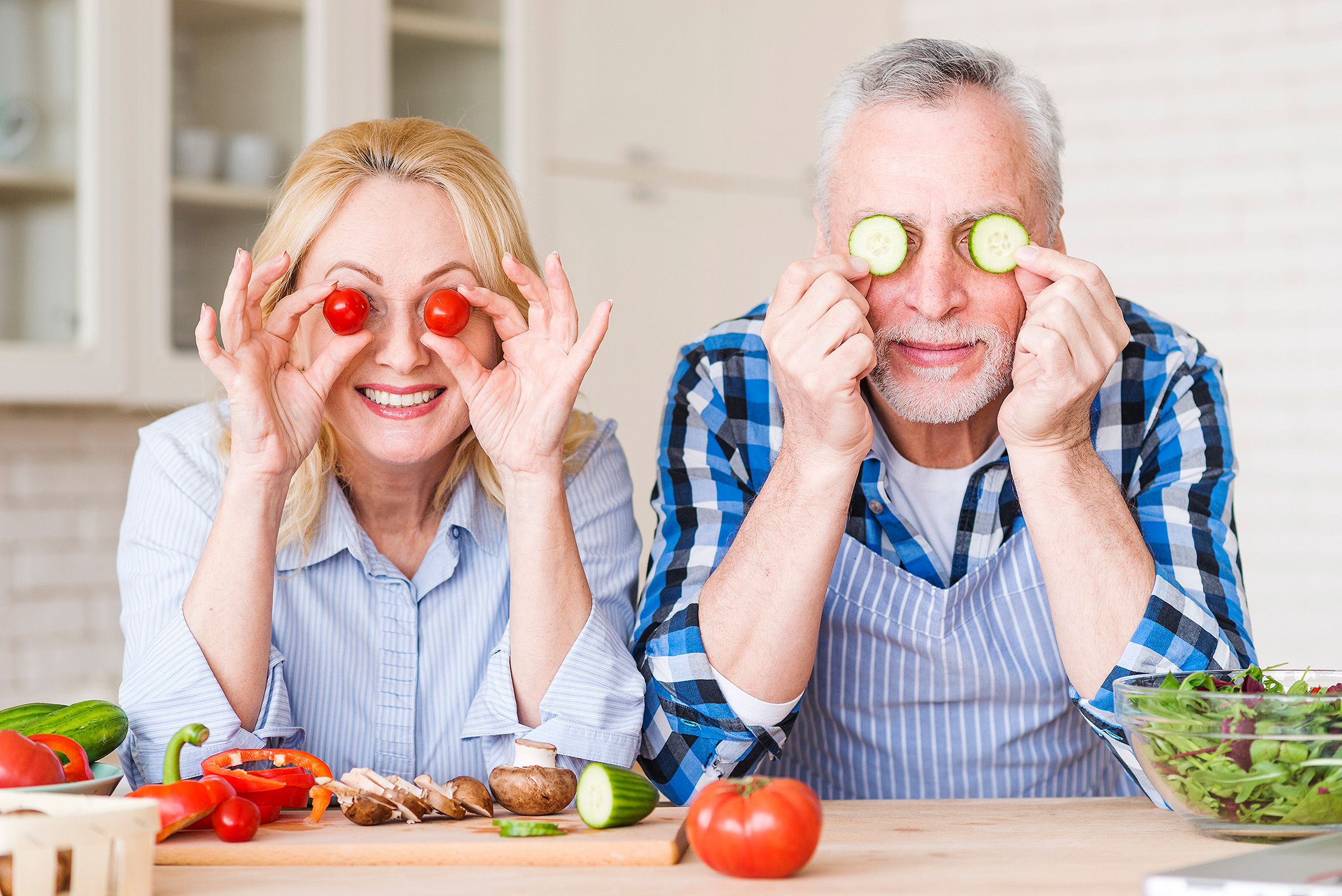 An elderly couple holding vegetables over their eyes. Showcasing nutritious foods for older adults