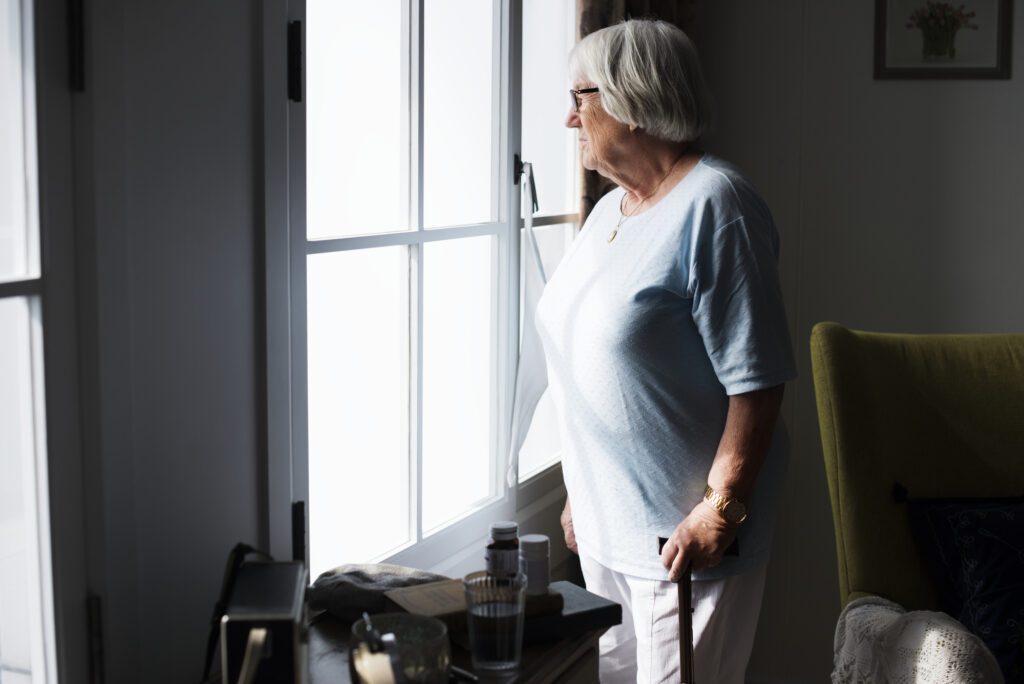 Senior woman standing by the window at home alone