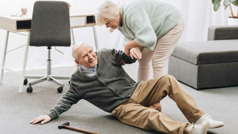 A senior man who has fallen to the ground being helped by a senior woman
